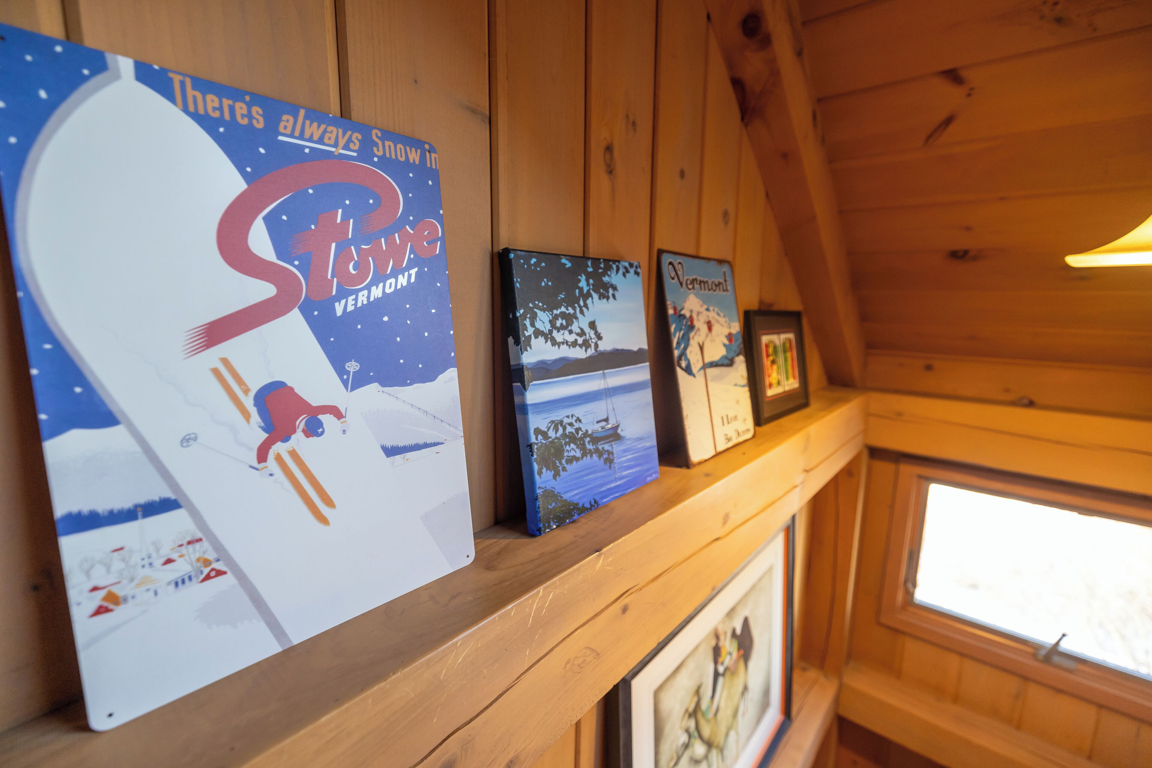 A wooden interior with a shelf displaying various framed artworks and a large poster.