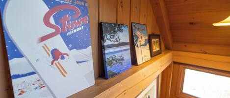 A wooden interior with a shelf displaying various framed artworks and a large poster.