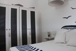 Une chambre à coucher avec un lit, une armoire noire et blanche, et une table de chevet sur laquelle se trouve un vase.