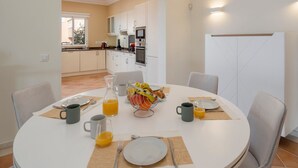 A dining area with a round table set for four, equipped with plates, cutlery, and a fruit bowl. - Palheiro Village villa, priv pool | Palheiro Ocean (São Gonçalo)