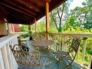 A covered outdoor area with a round metal table and two metal chairs, surrounded by a wooden deck and a white railing. - Comfort, Style, True Hospitality in the Heart of Old Louisville (Louisville)