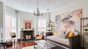 A living room with a fireplace, a sofa, a coffee table, and a chandelier. - Stylish Gem in the Heart of Old Louisville (Louisville)