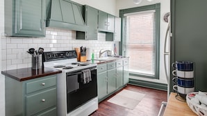 A kitchen with teal cabinets, a white stove, and a window with blinds. - Stylish Gem in the Heart of Old Louisville (Louisville)