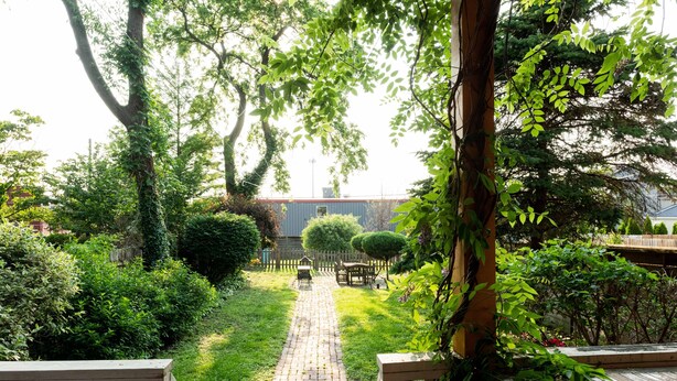 A garden pathway leading to a wooden deck with a table and chairs, surrounded by lush greenery and trees. - Stylish Gem in the Heart of Old Louisville (Louisville)