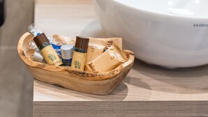 Una cesta de madera con distintos artículos de aseo sobre una mesa de madera, junto a un lavabo blanco.