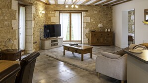 Una sala de estar rústica con paredes de piedra, una mesa de centro de madera, un sofá y un televisor sobre un mueble.