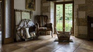 Una habitación con paredes de piedra, un ventanal grande, una silla y una cesta de mimbre.