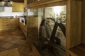 A kitchen with wooden cabinets, a granite countertop, and a large glass enclosure containing a mechanical gear. - Moulin du Fontcourt (Chasseneuil-sur-Bonnieure)