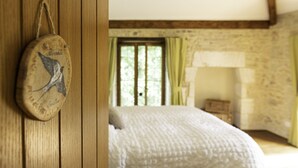 Una cama de madera rústica con colcha blanca, una pared de piedra y una ventana con cortinas.