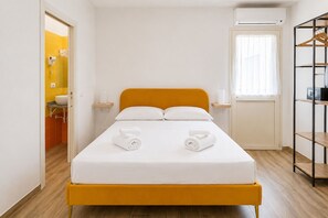 A hotel room with a bed, two rolled towels, a bedside table, a shelf, a wardrobe, and a window with curtains. - Palazzo Belmosto (Naples)