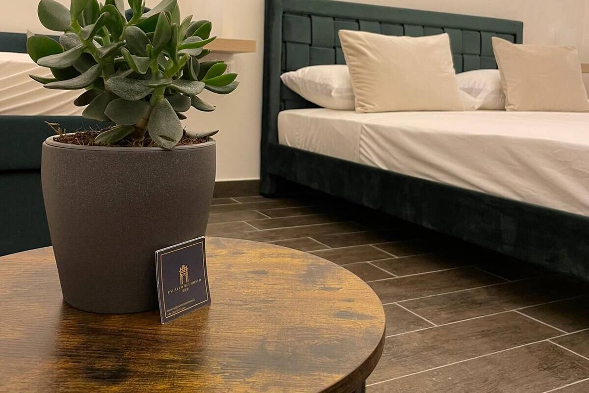 A room with a bed, a small round table with a potted plant, and a plaque on the table.
