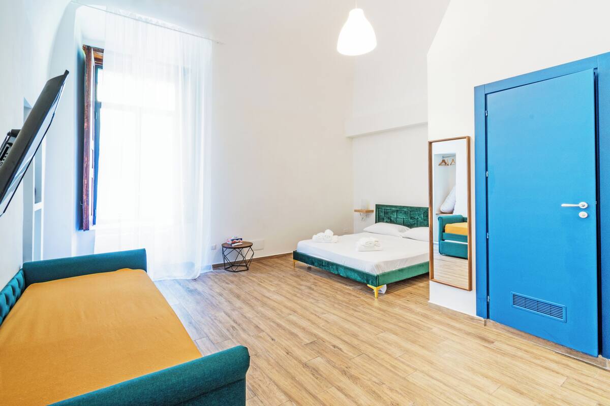 A modern hotel room with a bed, a desk, a chair, a wardrobe, and a window with curtains.