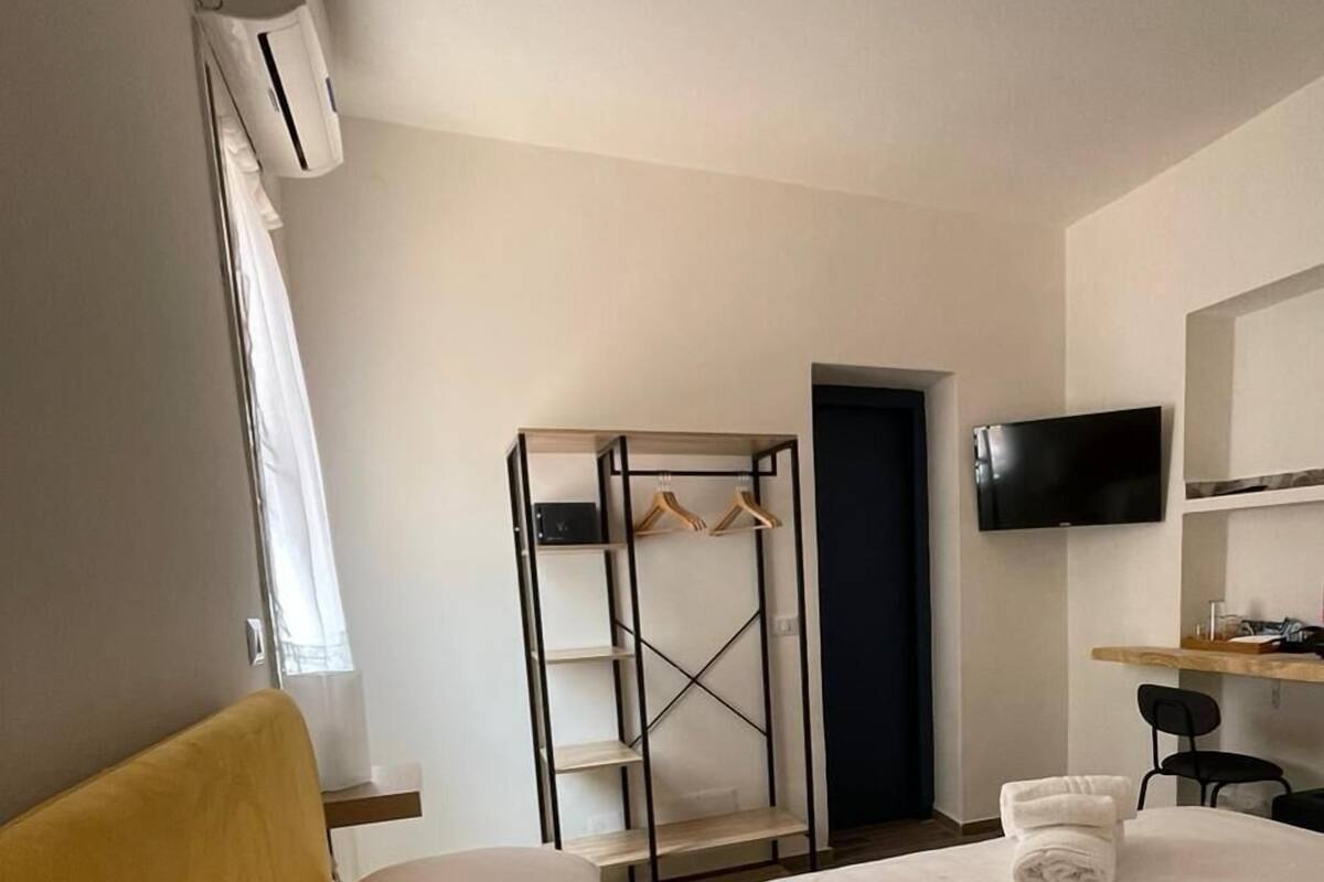A hotel room with a bed, a TV mounted on the wall, a wardrobe, and a desk with a chair.