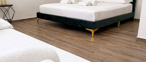 A modern hotel room with a neatly made bed, a small side table, and a wooden floor.