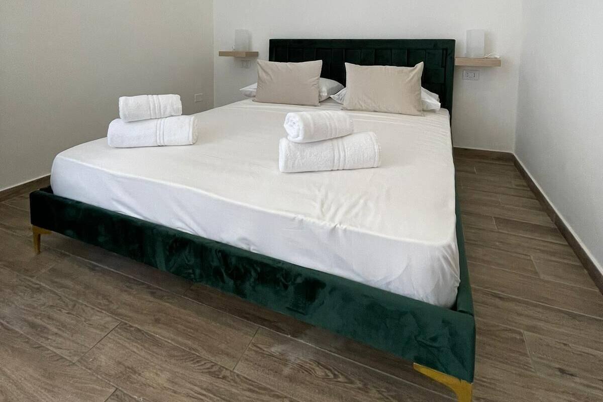 A neatly made bed with white linens and towels, a dark green headboard, and a wooden floor.