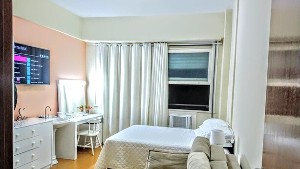 A hotel room with a bed, a desk with a chair, a dresser, and a window with curtains. - Ap Copacabana 200m da praia - CP5 (Rio de Janeiro)