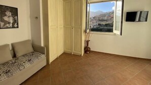 A room with a sofa, a wardrobe, a window with a view of a town, and a flat-screen TV. - Chez Luke Apartment "Vintage" , 10 minutes from "Path of the God" (Pianillo)