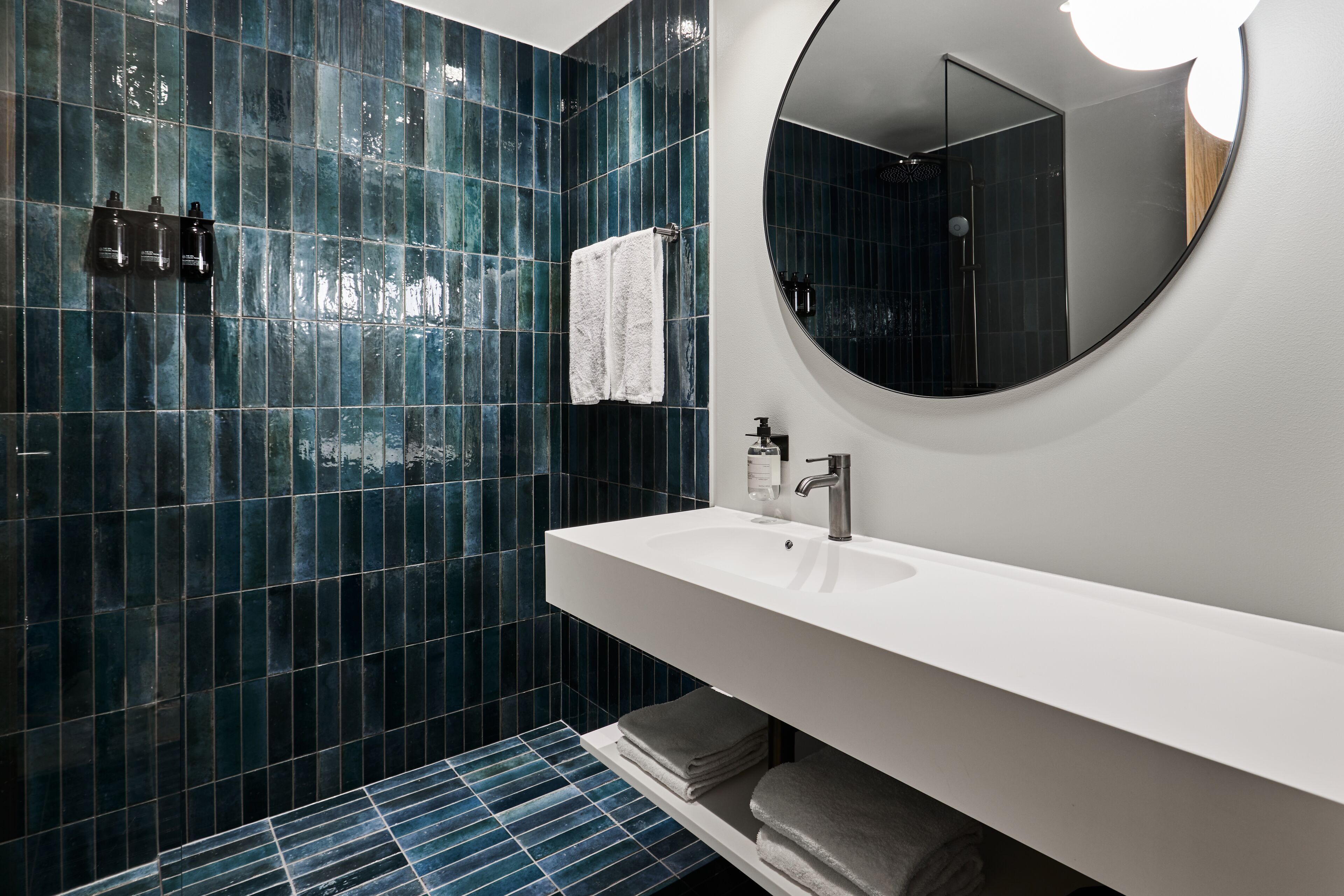 A modern bathroom with a white sink, a round mirror, and blue-tiled walls.