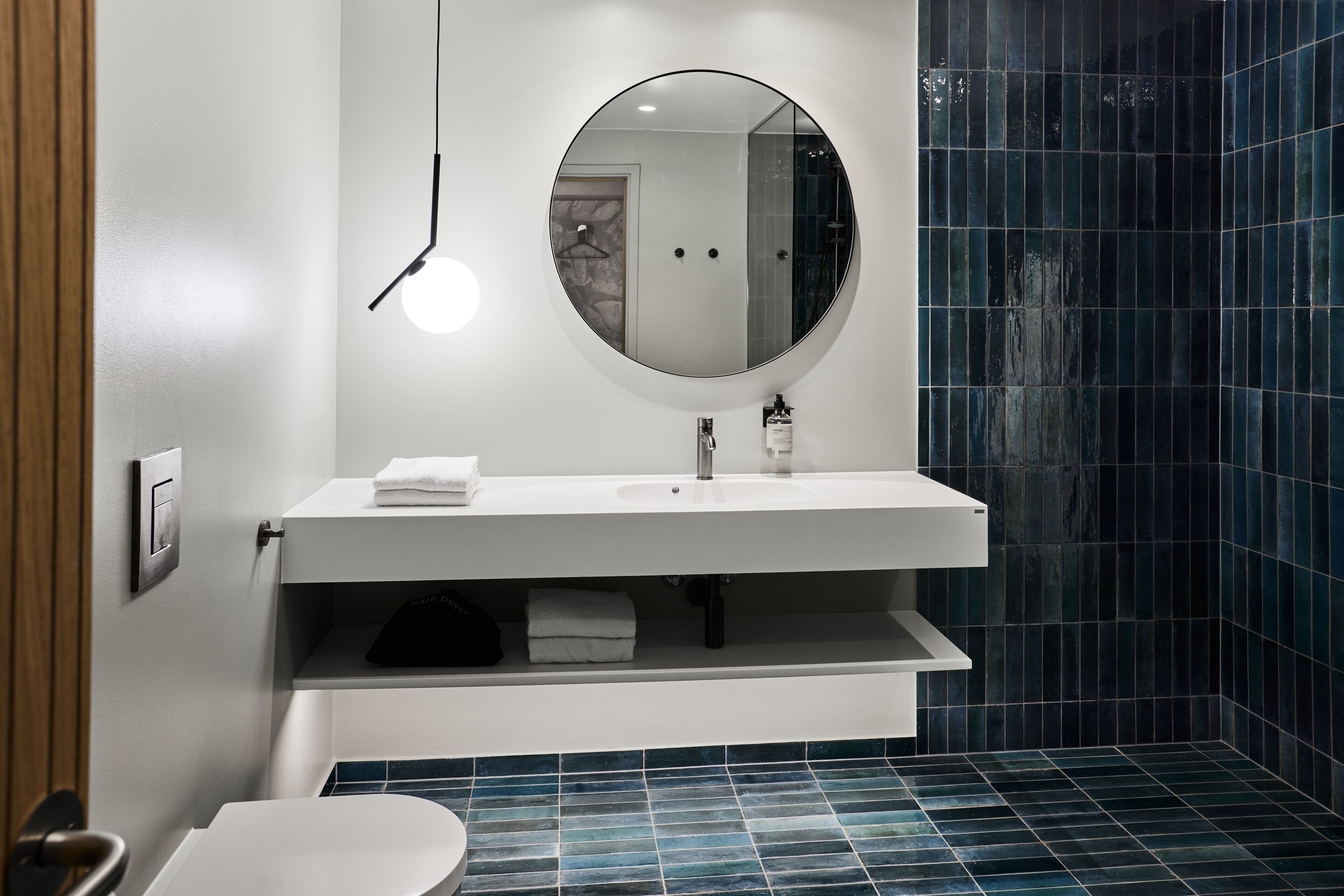 Un baño moderno con un espejo redondo, lavamanos blanco y paredes con azulejos azules.