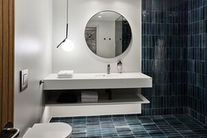 Un baño moderno con un espejo redondo, lavamanos blanco y paredes con azulejos azules.