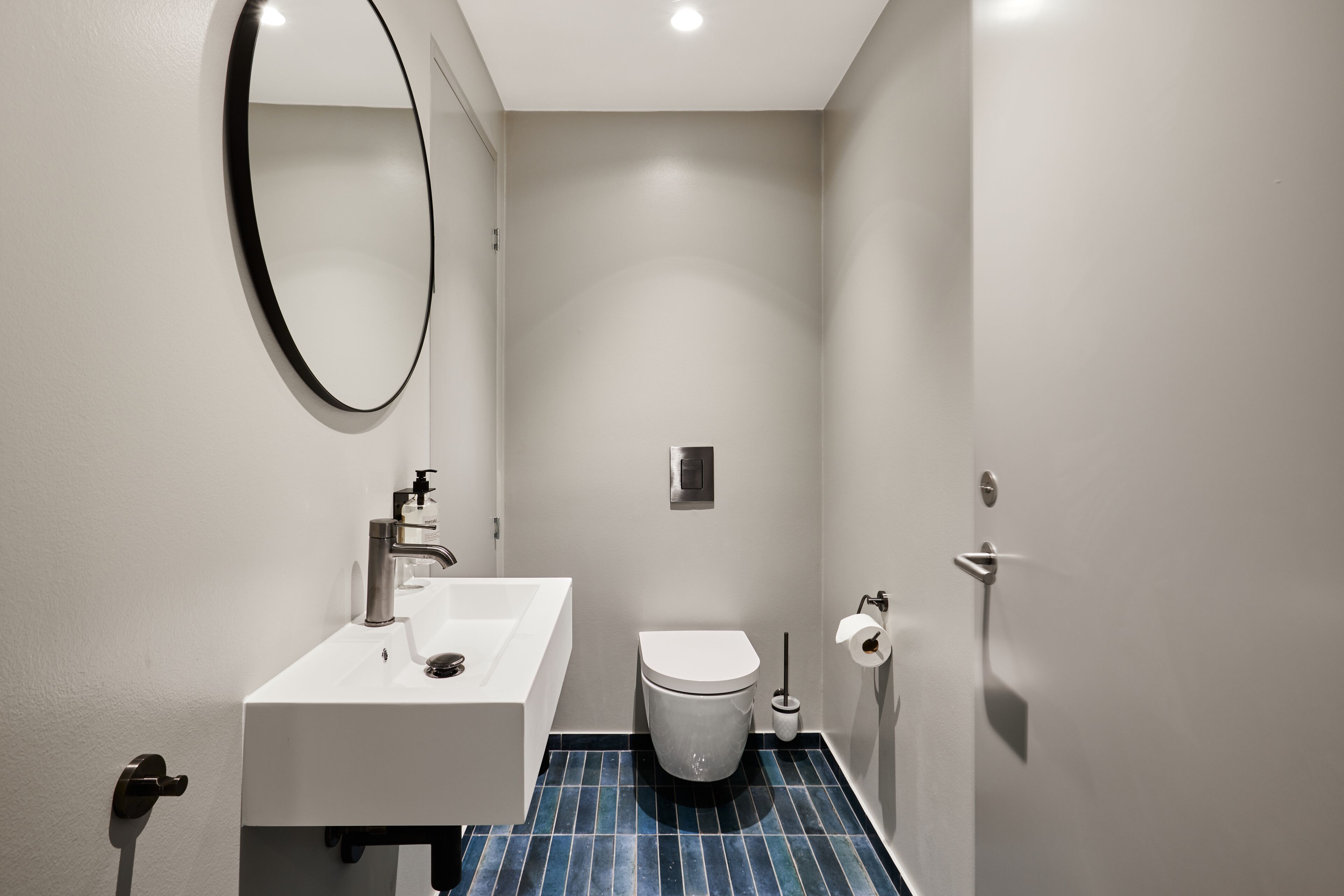 Un baño pequeño y moderno con un lavamanos blanco, un inodoro y un espejo.