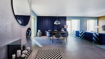A modern living room with a dining area, featuring a round mirror, a glass coffee table, and a striped rug.