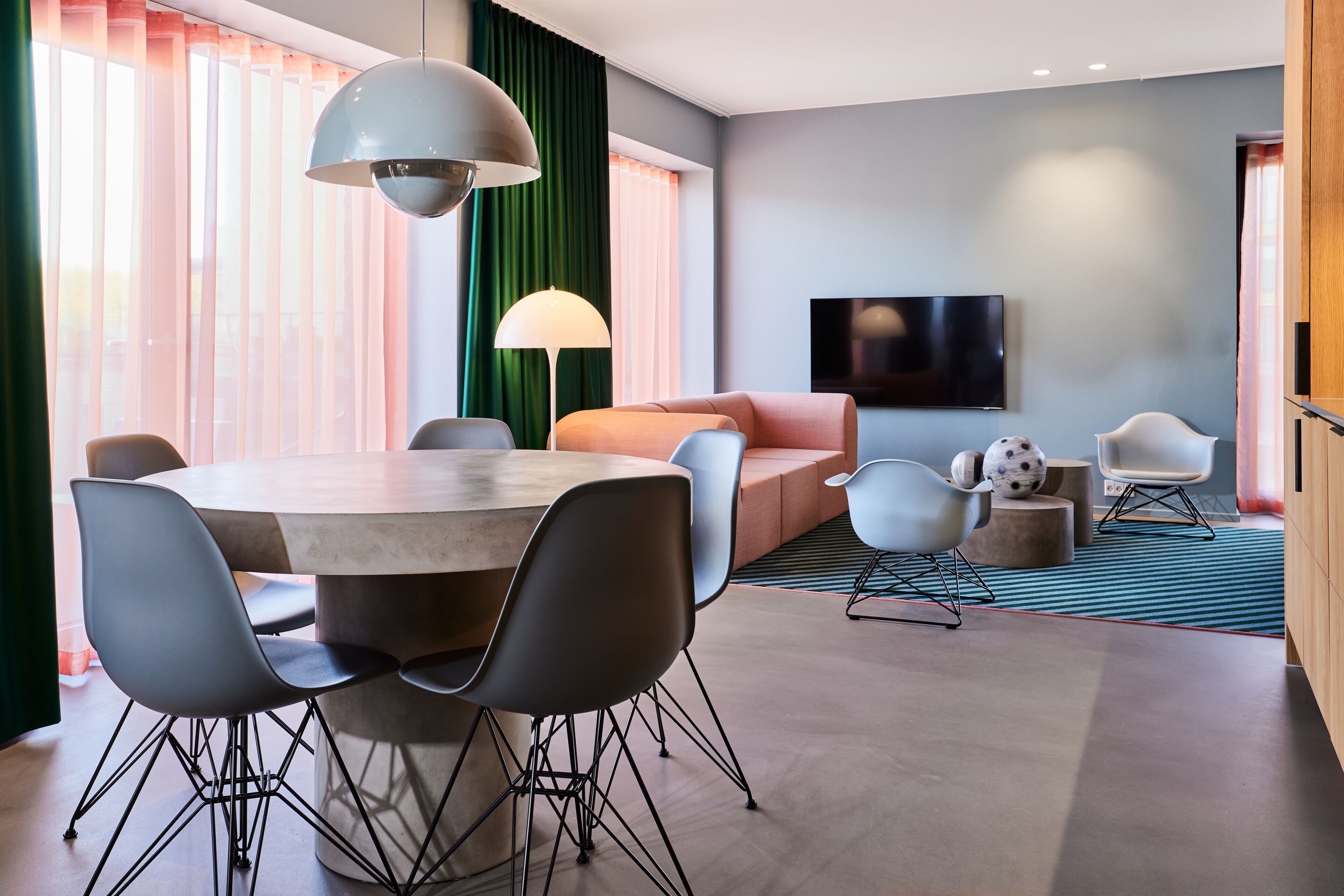 A modern hotel room with a dining area, a sofa, a TV, and a large window with curtains.