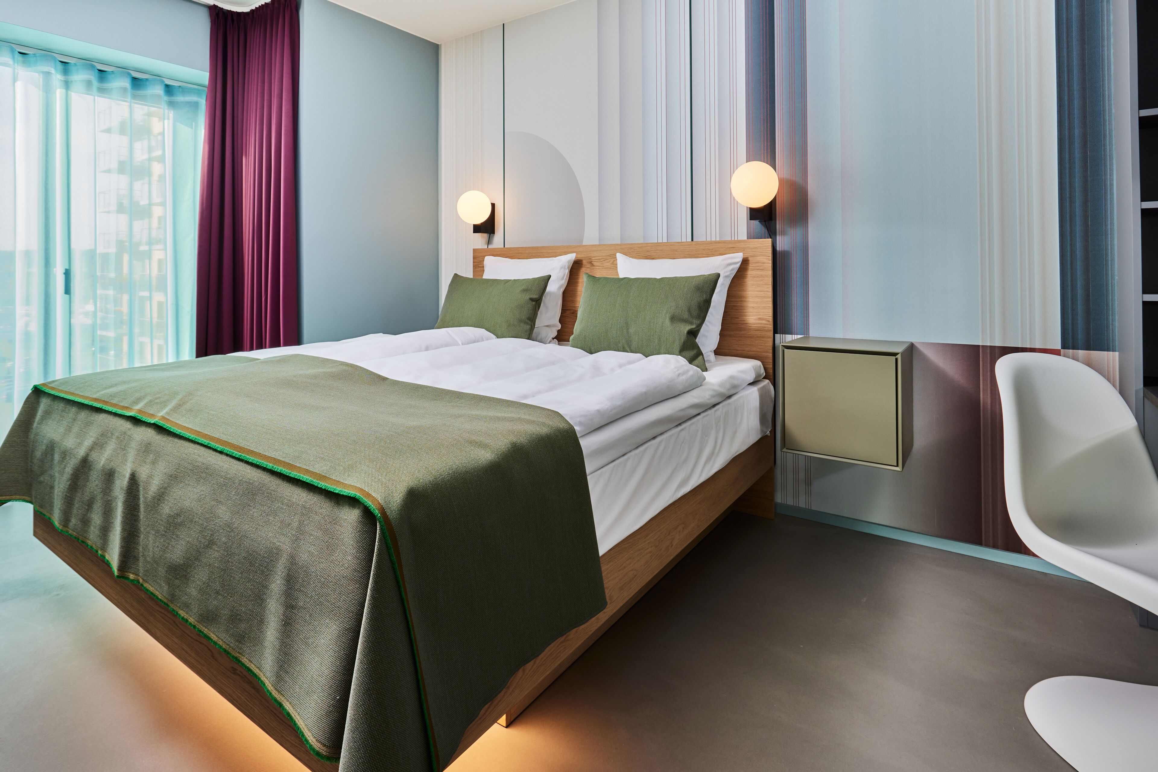 A modern hotel room with a large bed, a desk, and a chair.