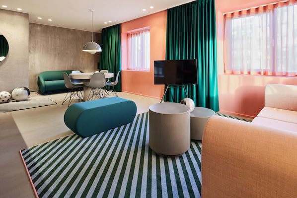 Un salon moderne avec un canapé, un pouf et un téléviseur à écran plat.