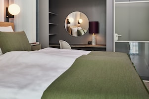 Una habitación de hotel con una cama grande, un espejo redondo, un escritorio con una lámpara y una silla.