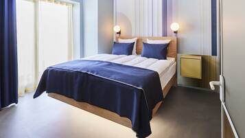 A modern hotel room with a large bed, bedside tables, and a nightstand.