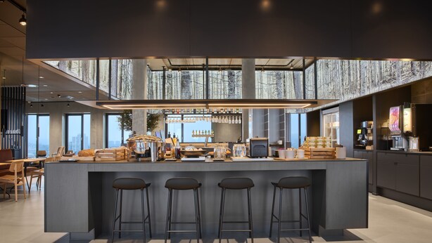 A modern kitchen with a central island, bar stools, and a high ceiling with a view of the city. - Kirk Suites (Vejle)