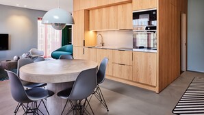 A modern kitchen with wooden cabinets, a built-in oven, and a round dining table with chairs. - Kirk Suites (Vejle)
