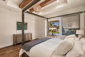A bedroom with a large bed, a wooden dresser, and a view of a swimming pool.