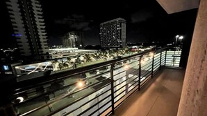 Une vue nocturne depuis un balcon donnant sur un paysage urbain, avec des bâtiments modernes et une rue bien éclairée en contrebas.