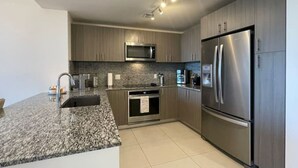 Une cuisine moderne dotée de plans de travail en granit, d’appareils électroménagers en acier inoxydable et d’armoires en bois.