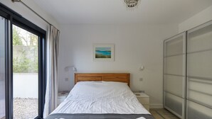 Une chambre à coucher comprenant un lit, une table de chevet, une commode, une fenêtre, une porte et un lustre.