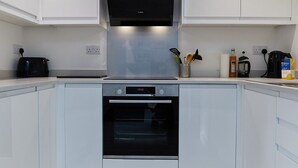 Une cuisine moderne avec des meubles blancs, une hotte en acier inoxydable, un four et une machine à café.