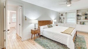 Ein Schlafzimmer mit einem hölzernen Bett, Nachttischen, einem Deckenventilator und einem Fenster mit Jalousien.