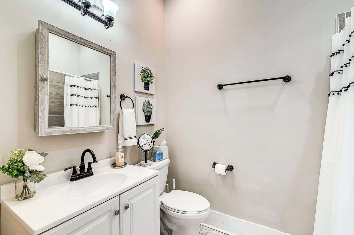 A bathroom with a white sink, mirror, toilet, and shower curtain.