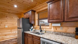 A kitchen with wooden walls, a stainless steel refrigerator, a dishwasher, granite countertops, and wooden cabinets. - Stunning Views,Hot Tub, Game Room,Zero Stair Entry (Cosby)