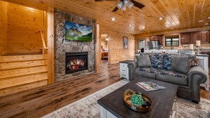A cozy cabin interior with a fireplace, wooden walls, a sofa, and a dining area. - Stunning Views,Hot Tub, Game Room,Zero Stair Entry (Cosby)