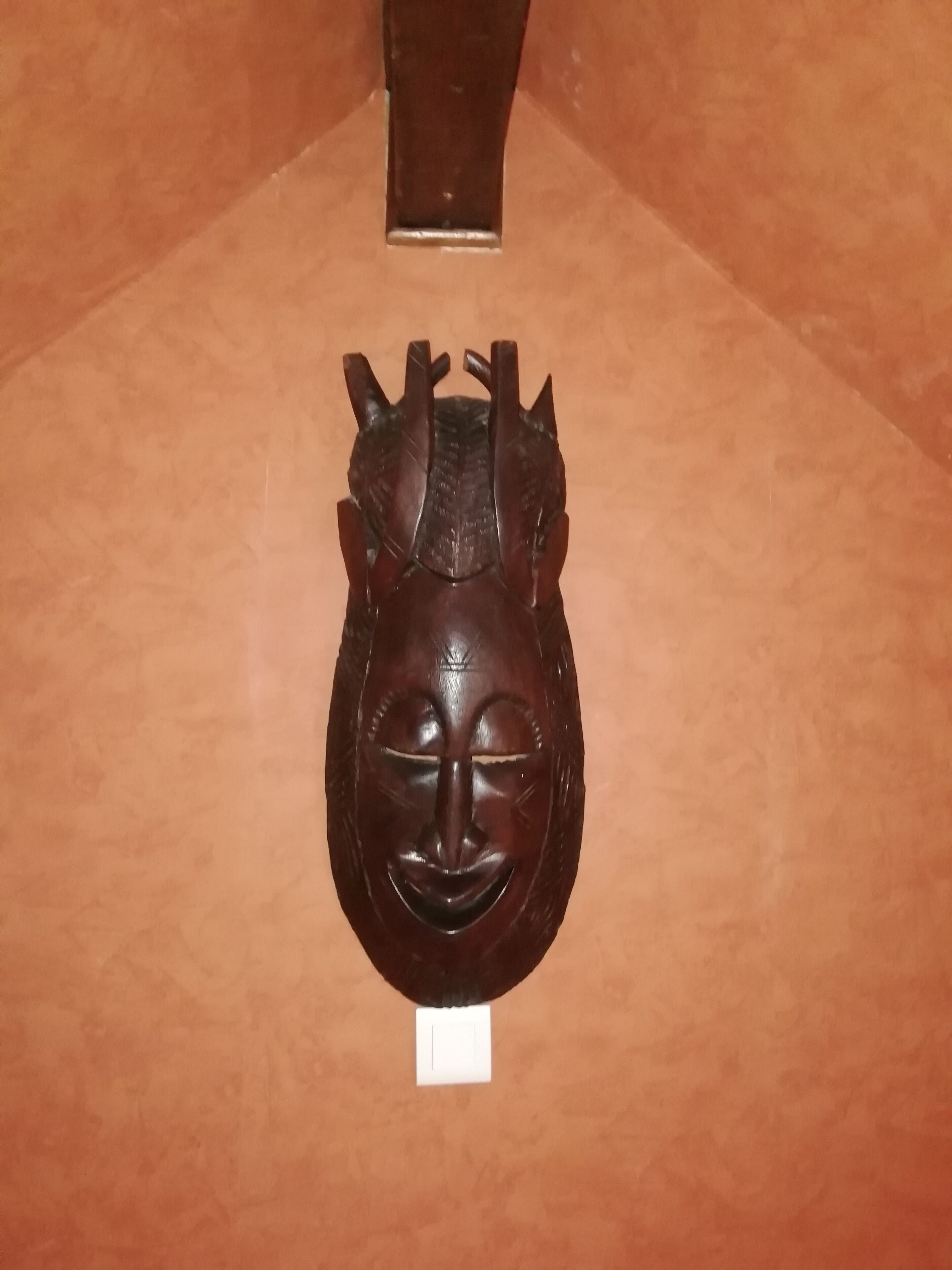 Un masque en bois, de forme rectangulaire, avec une petite étiquette blanche placée en dessous.