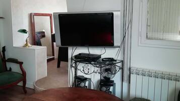 Un salon avec une table en bois, un téléviseur, des haut-parleurs et un radiateur.
