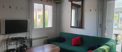 Una habitación con un sofá verde, una mesa de madera, un televisor y un espejo.