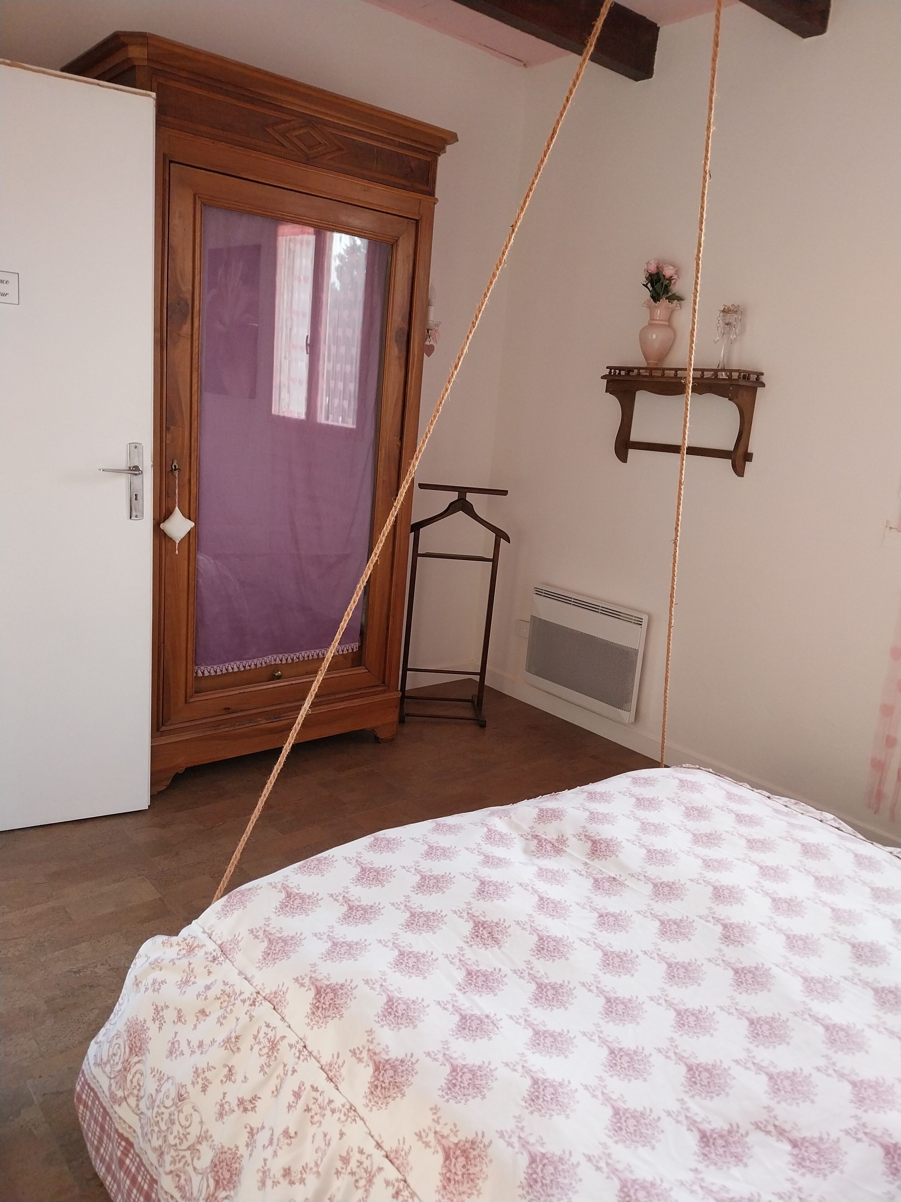 Une chambre à coucher comprenant un lit, une armoire, un radiateur et une petite étagère sur laquelle est posé un vase.