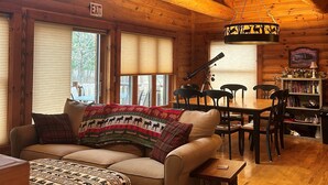 A cozy cabin interior with a wooden ceiling, a sofa with patterned blankets, a dining table with chairs, and a bookshelf. - Family Friendly Deep Water Getaway - Close to Sand Valley Golf Courses (Nekoosa)