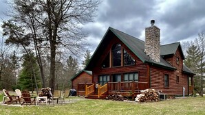 A log cabin with a stone chimney, wooden deck, and outdoor seating area. - Family Friendly Deep Water Getaway - Close to Sand Valley Golf Courses (Nekoosa)