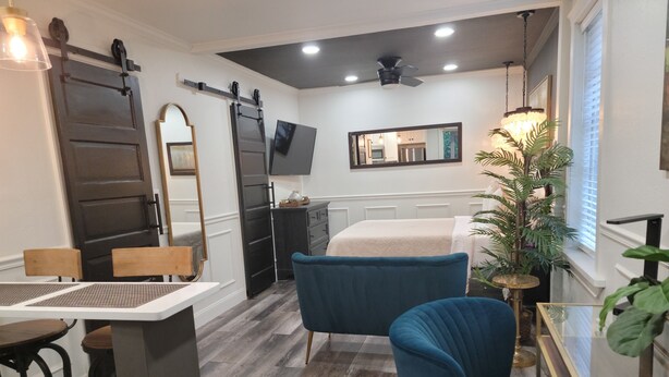 Una habitación pequeña con cama, escritorio, silla, televisión y un espejo grande.