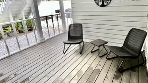 Un espacio al aire libre techado con dos sillas de mimbre y una mesa pequeña, un techo blanco con diseño de cuadrícula y una pared con un diseño de árbol circular y dos aves.